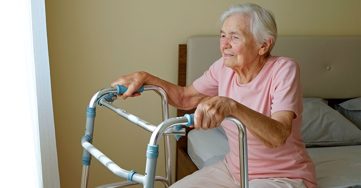 Seniorin sitzt auf einem Bett und hält sich am Rollator fest | Umzug ins Pflegeheim