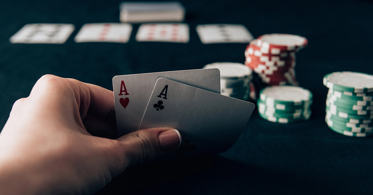 Eine Pokerspielerin sitzt am Pokertisch mit Chips und hält zwei Asse in der Hand als Symbol für eine gute Verhandlungsposition in der Preisverhandlung beim Immobilienkauf | Immobilienkauf